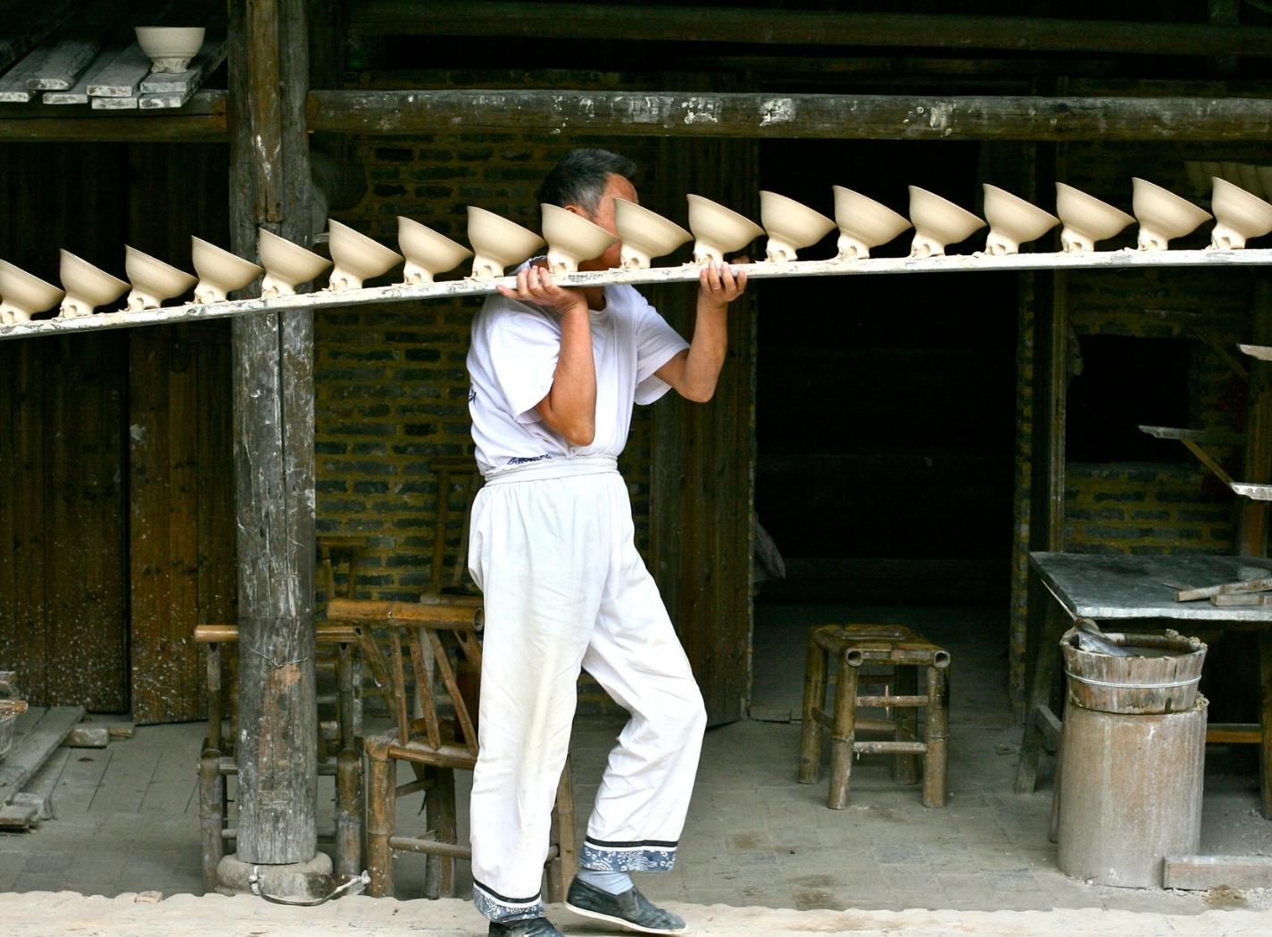 Operaio trasporta una fila di ciotole in ceramica ancora grezza a Jingdezhen