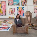 Rubi Nery seduta nel suo studio, circondata da dipinti e sculture ceramiche figurative