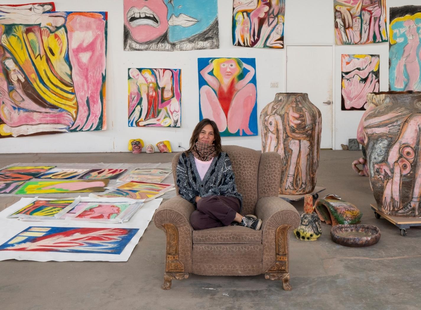 Rubi Nery seduta nel suo studio, circondata da dipinti e sculture ceramiche figurative