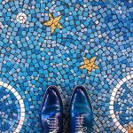 Pavimento a mosaico azzurro con stelle gialle e archi bianchi, fotografato dall'alto con un paio di scarpe blu