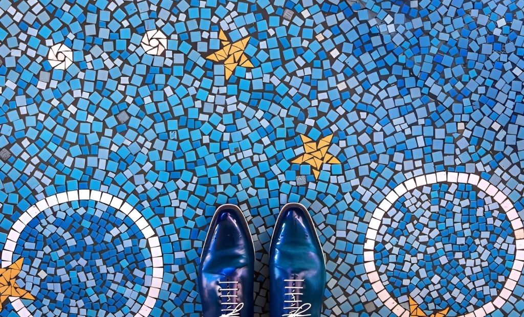 Pavimento a mosaico azzurro con stelle gialle e archi bianchi, fotografato dall'alto con un paio di scarpe blu