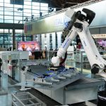 Braccio robotico industriale bianco al lavoro su una linea di movimentazione lastre in un padiglione fieristico