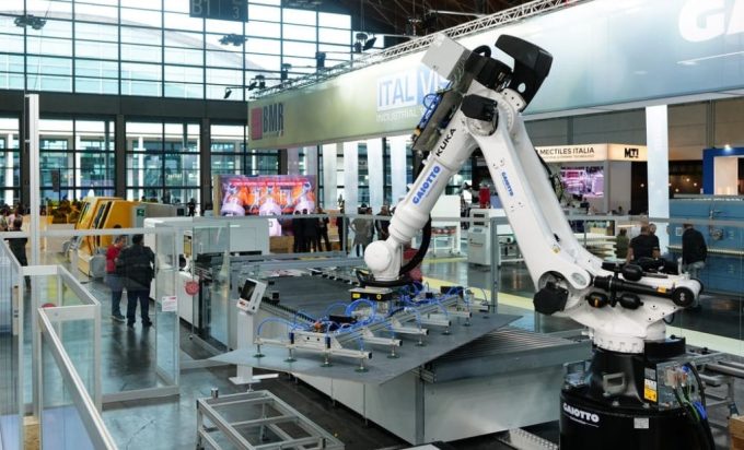 Braccio robotico industriale bianco al lavoro su una linea di movimentazione lastre in un padiglione fieristico