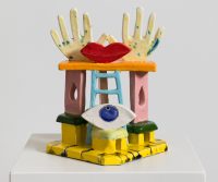 Scultura in ceramica colorata con mani, occhio e labbra rosse su una struttura geometrica